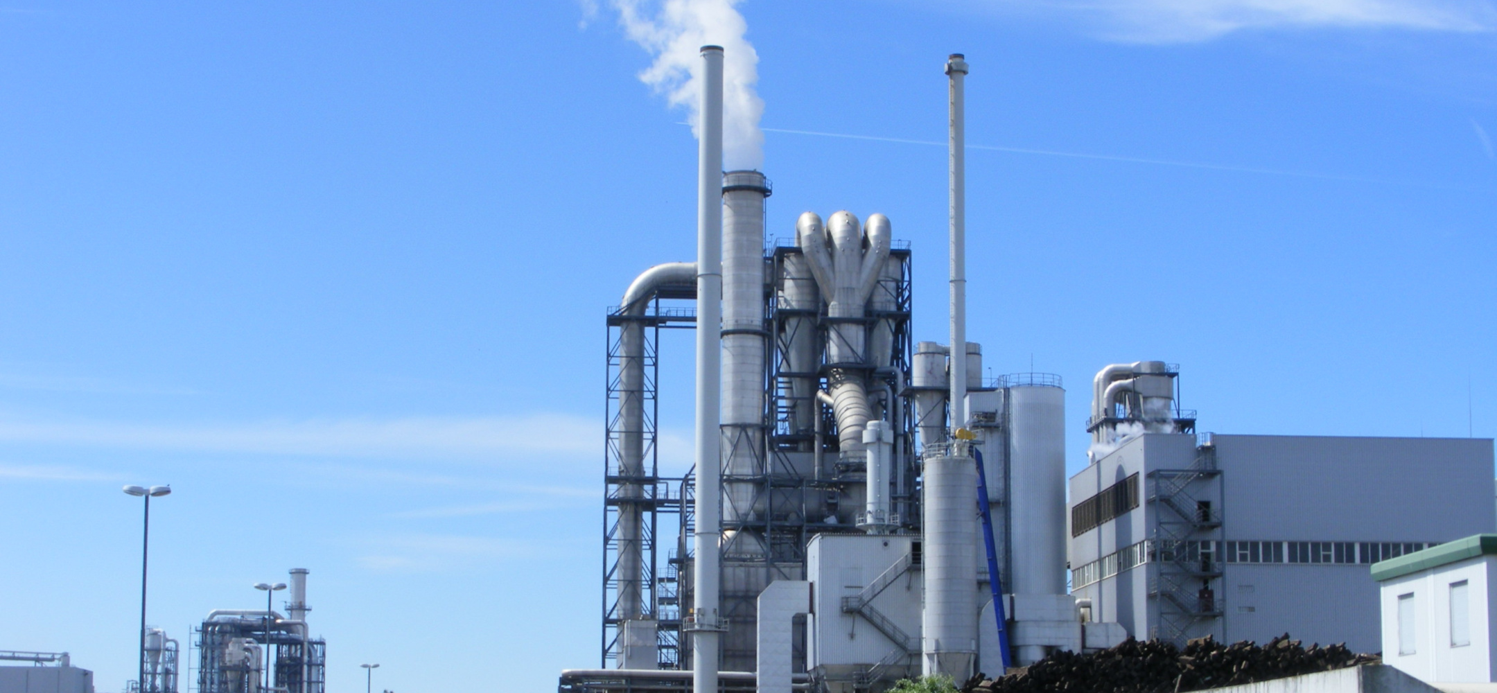 Blick auf ein funktionales, mehrstöckiges Industriegebäude mit Schornsteinen und komplexem Rohrsystem.